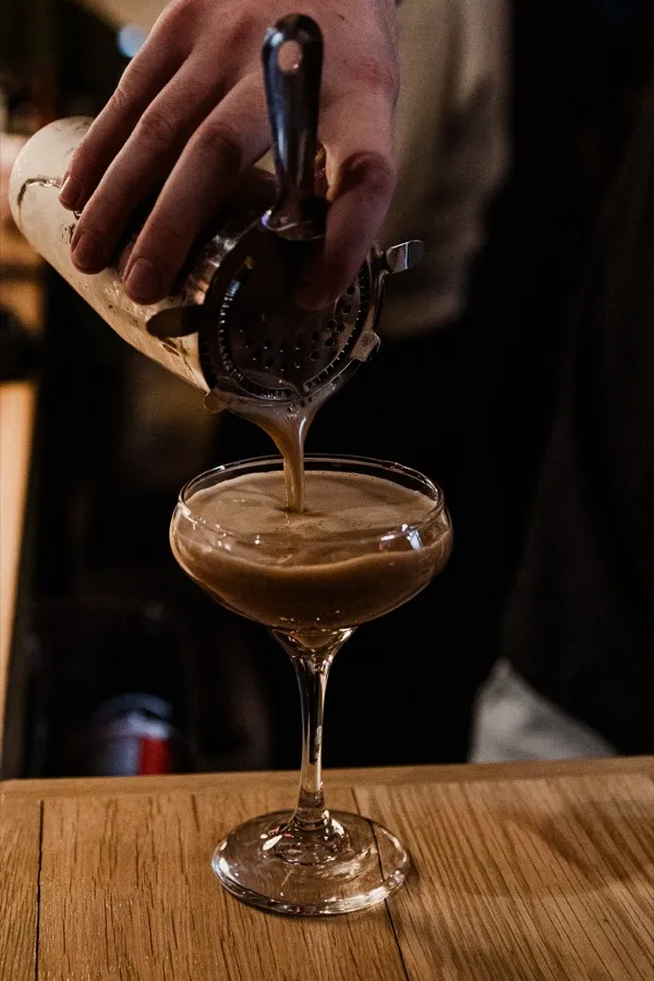 A bartender straining an espresso martini into a coupe glass