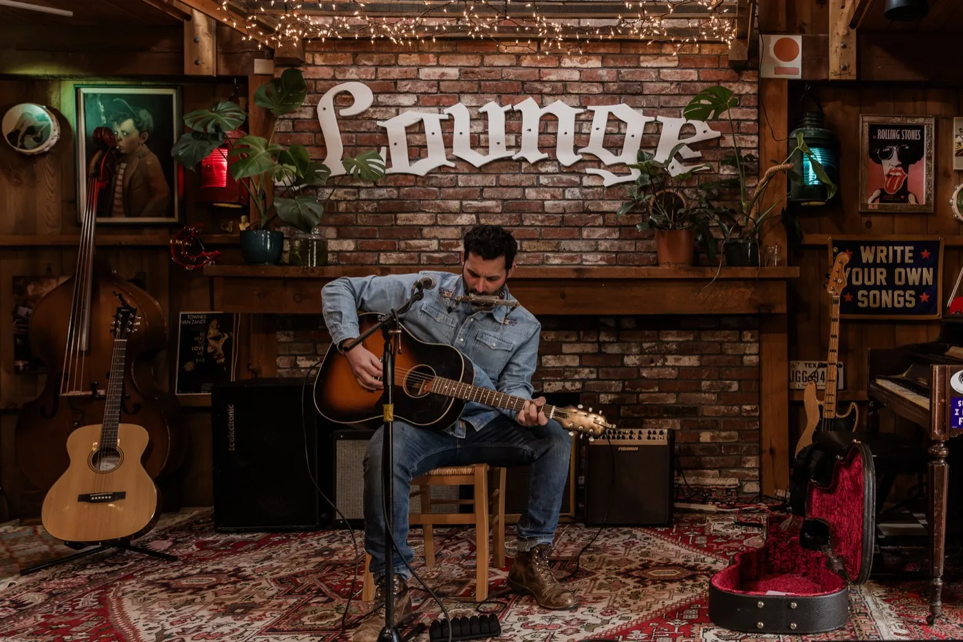 A solo guitarist and harmonica player in front of the brick wall and Lounge sign